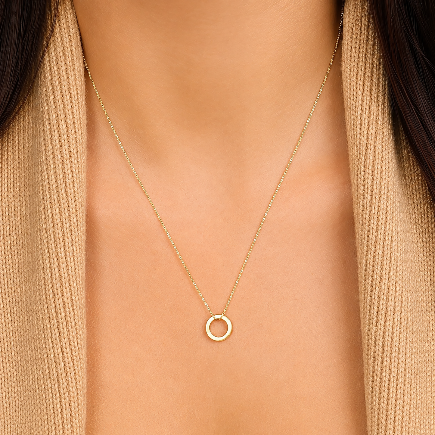 Gold necklace with a small round pendant on a person wearing a beige sweater.